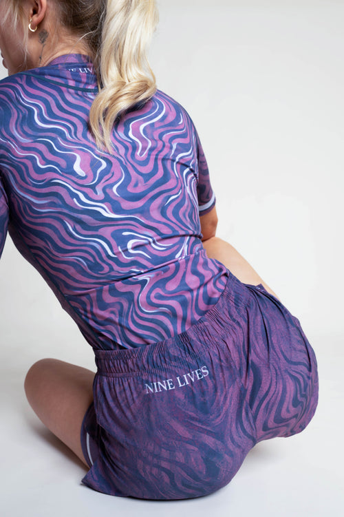 Person wearing a purple patterned outfit with 'Nine Lives' branding on a white background
